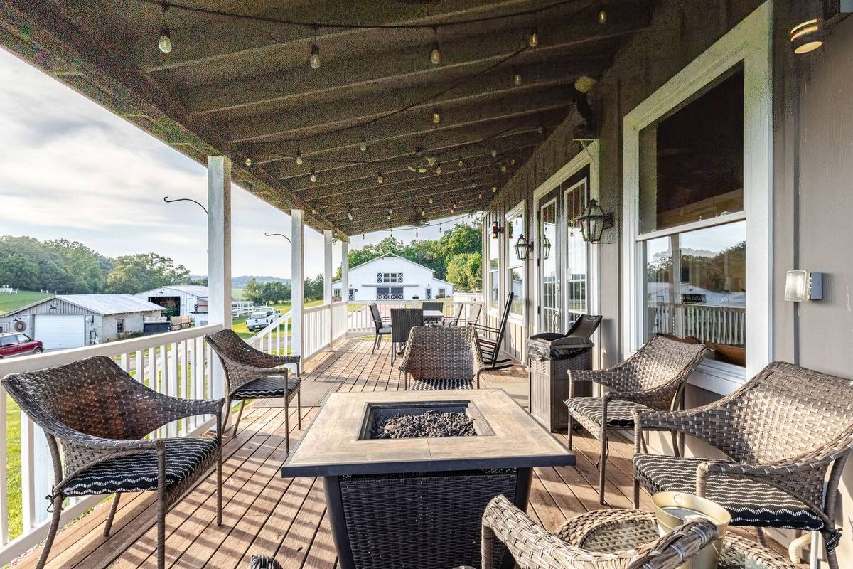 Milkbarn front covered porch with fire pit, wicker seating, gas lanterns, and bistro lighting