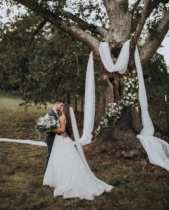 A bride beneath the Big Oak Tree draped in white fabric and florals at a farm wedding near Gatlinburg