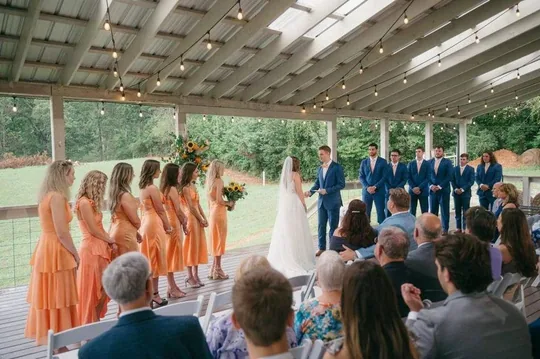 A wedding ceremony under the covered Grand Veranda with bistro lights and farm views in the Smoky foothills