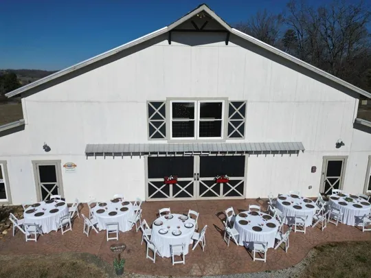The Grand White Barn with round reception tables set on the front patio, the reception space for a Tennessee farm wedding near Sevierville