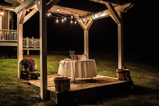 The Main Stage arbor glowing under string lights at night, curved steps leading up, at Cedar Pond Farms