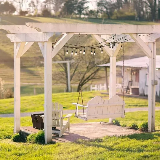 A white Pond Side Swing Arbor with porch swing and string lights at golden hour