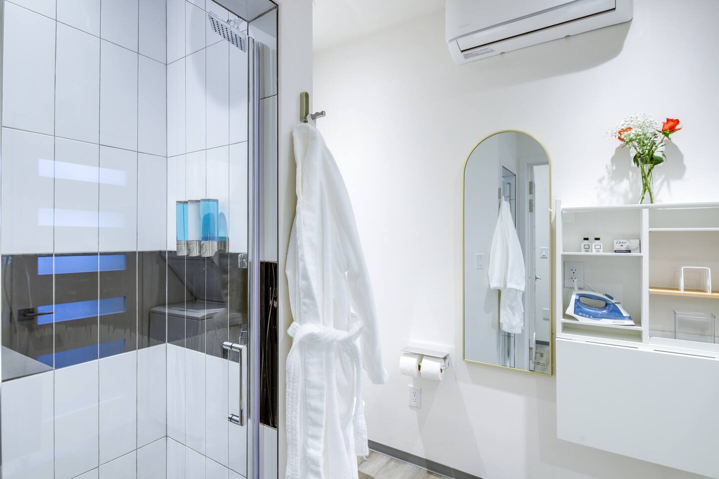 A full bath with a two head tile shower, indirect lighting, washer and dryer combo, suspended wash sink.